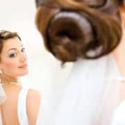 Braut mit Hochsteckfrisur betrachtet sich im Spiegel