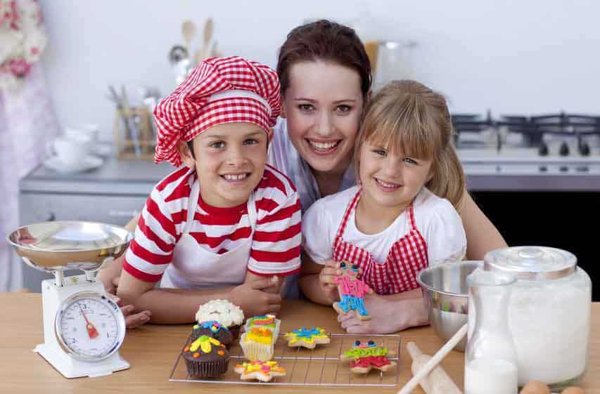 Mutter und zwei Kinder mit Backutensilien in der Küche lächeln in die Kamera